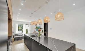 Een moderne keuken met een marmeren aanrechtblad, hanglampen en uitzicht op het buitengebied.