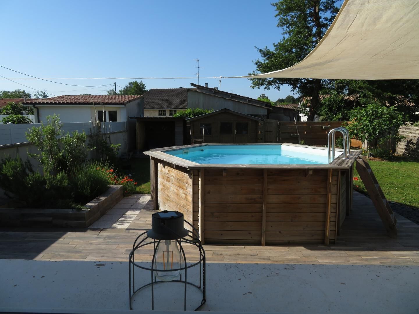 Un bain à remous en bois, équipé d’une échelle, entouré d’une cour arrière agrémentée d’une terrasse en bois, d’un petit tabouret et d’un grand auvent.