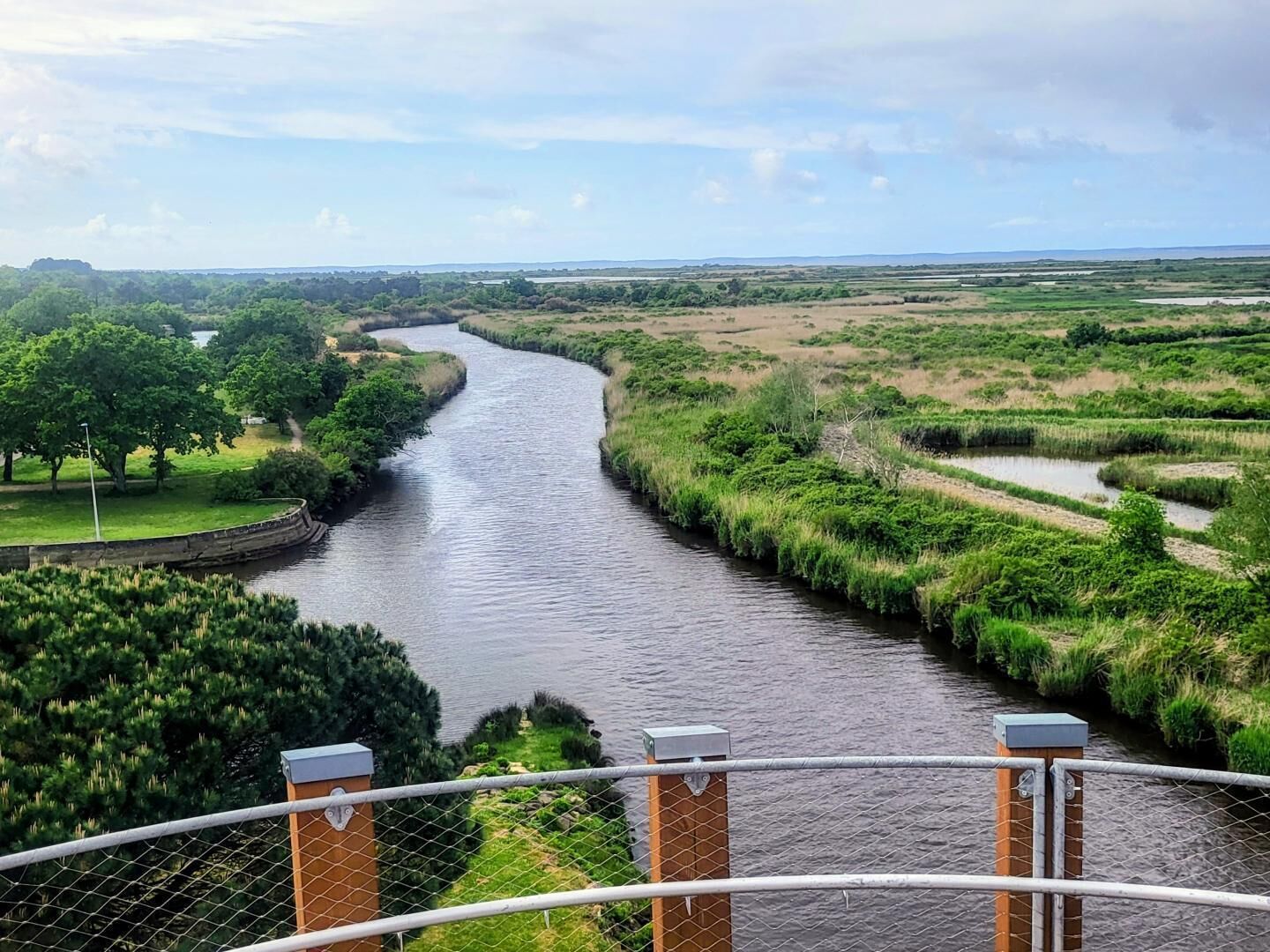 A river with a fence in the foreground and a view of the landscape beyond.