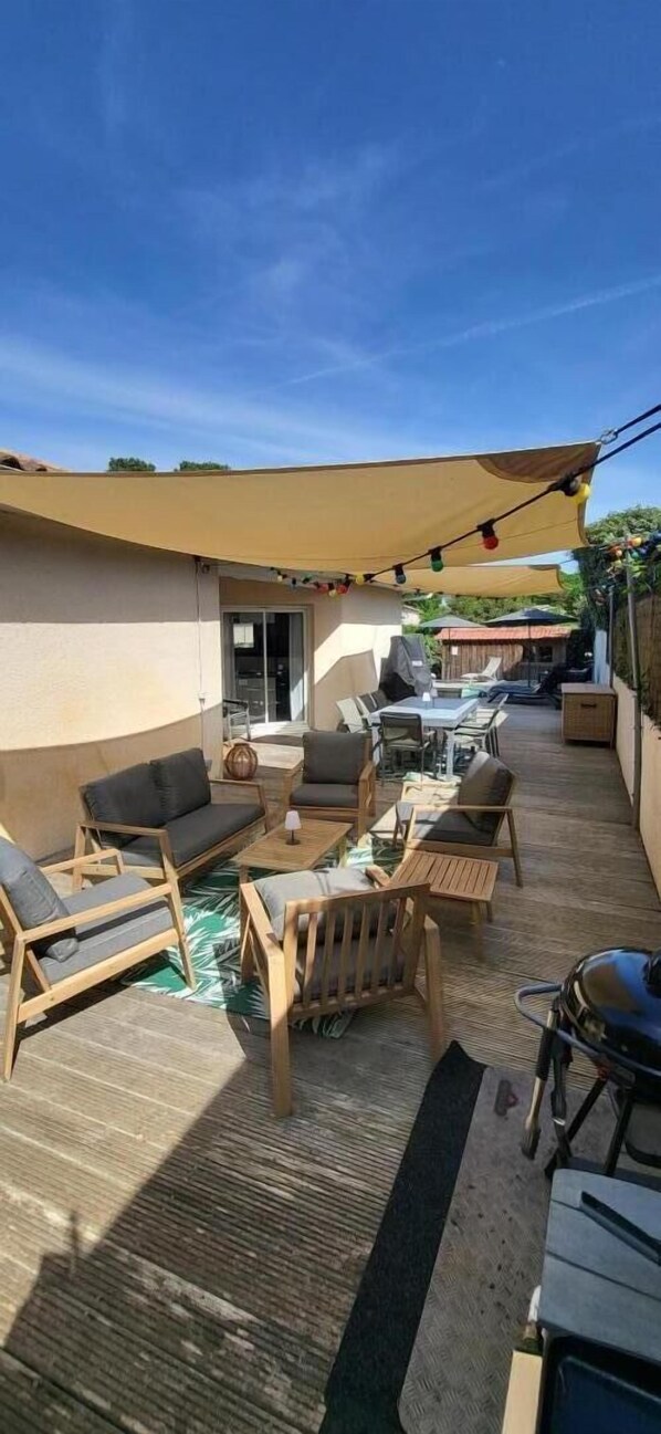Une terrasse extérieure avec des meubles en bois, un barbecue et un espace salon abrité.