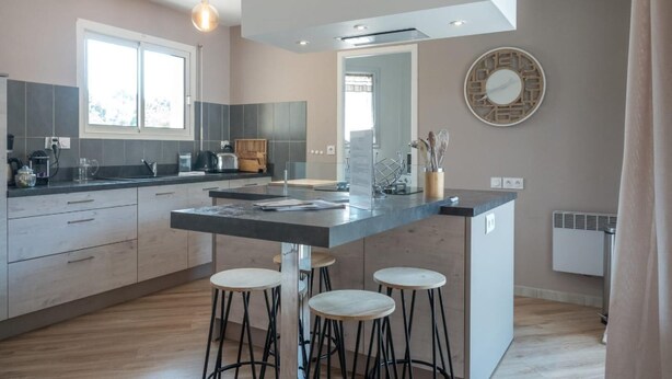 Une cuisine moderne dotée d’un îlot central, de tabourets de bar, d’un grand miroir et d’une enseigne « PAGAYO ».