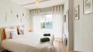 Une chambre à coucher avec un grand lit, une tête de lit en bois, des rideaux blancs et une vue sur un jardin par la fenêtre.