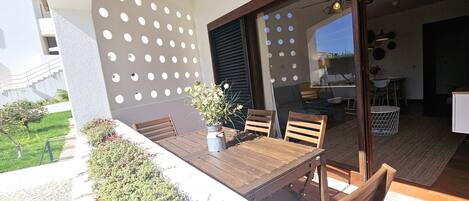 An outdoor patio with a wooden table and chairs, a potted plant, and a wall with circular cutouts.