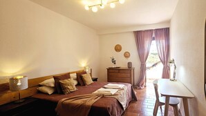 A hotel room with a bed, bedside tables, a desk, and a chair. There are curtains, a lamp, and wall decorations.