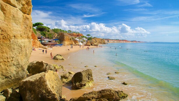 A beach with rocky formations, clear blue water, and a few people enjoying the beach.