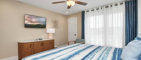 A bedroom with a bed, a ceiling fan, a TV, a dresser, and a window with curtains.