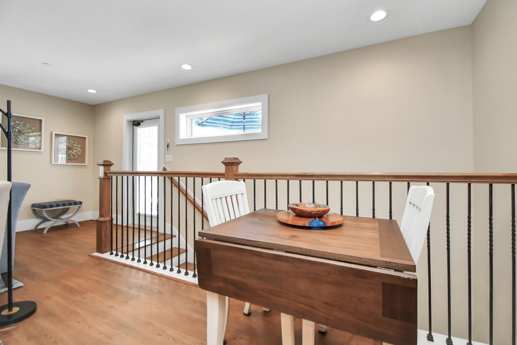 A dining area with a wooden table and chairs, a staircase with a railing, and artwork on the walls.