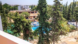 En vy över ett hotell med en pool omgiven av träd, en parkeringsplats och en stadsbild i fjärran.