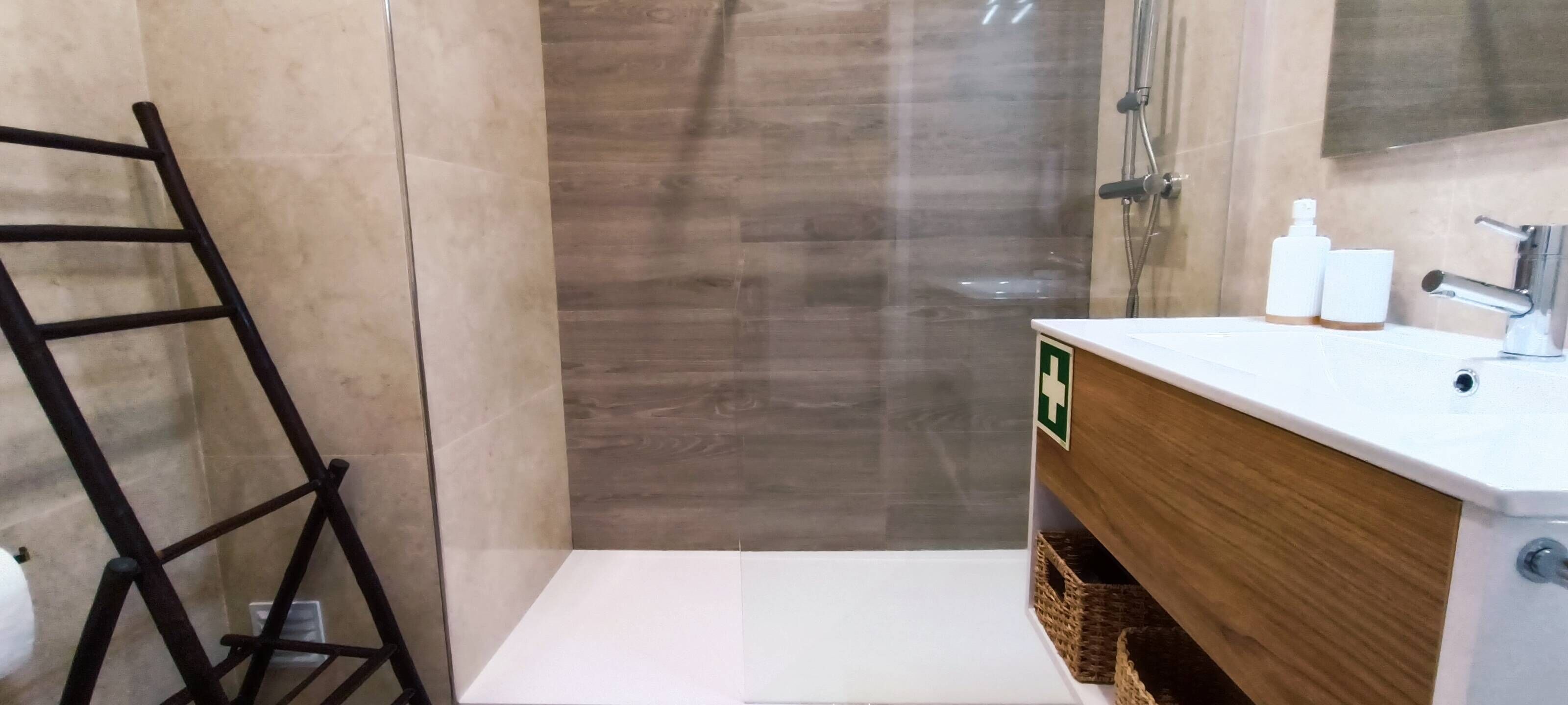 Un bagno con doccia, un mobile contenitore in legno e un porta asciugamani.