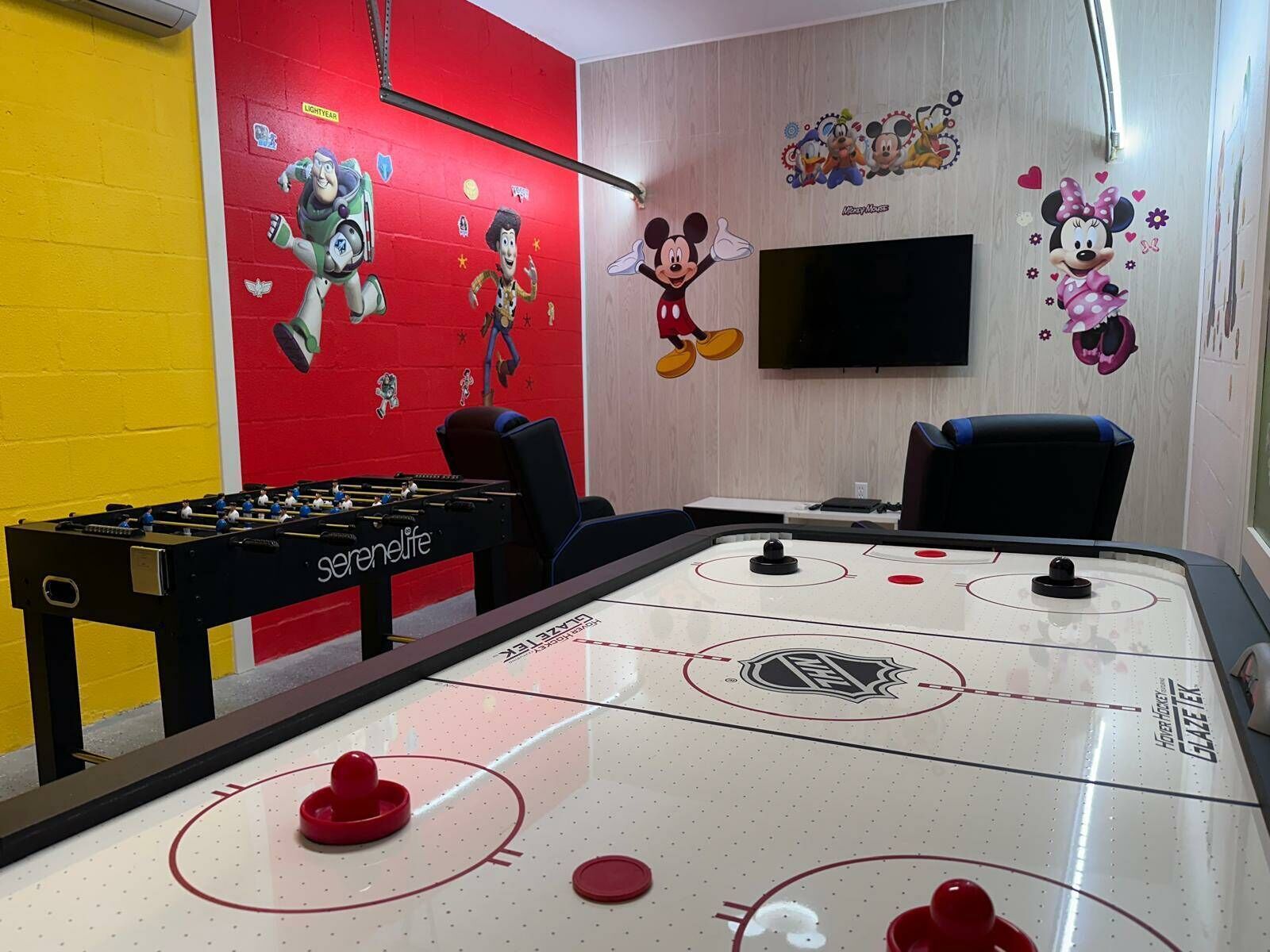 A room with a foosball table, a table tennis table, and a television.