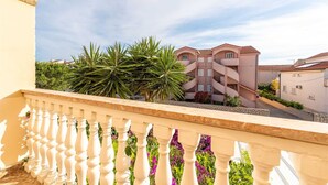 Ein Balkon mit weißer Brüstung, der auf ein Gebäude mit rosa Fassade und mehreren Balkonen blickt.