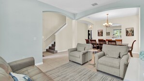 A spacious living room with a high ceiling, a staircase, and a dining area with wooden furniture.