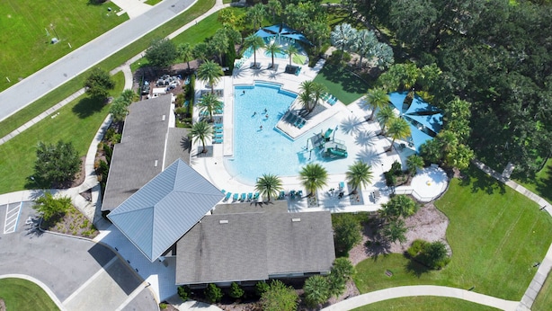 An aerial view of a resort with a large swimming pool, palm trees, and a building with a sloped roof.