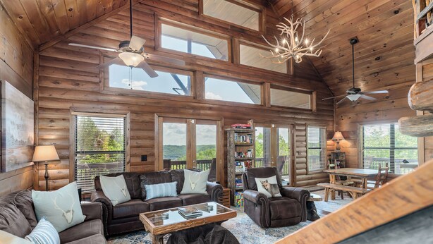 A spacious log cabin interior with a large living area, multiple seating options, and a view of the outdoors. - Fox & Bear Lodge Near Center Hill Lake (Smithville)