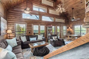 Un interior espacioso de cabaña de troncos con un amplio salón, varias opciones de asientos y vistas al exterior.