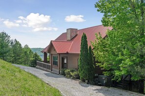 Une cabane en rondins avec un toit rouge, une allée en gravier et une vue sur la forêt environnante.