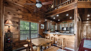 A wooden cabin interior with a dining area, kitchen, and a large window. - Fox & Bear Lodge Near Center Hill Lake (Smithville)