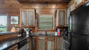 A kitchen with wooden cabinets, a black refrigerator, and a window with blinds. - Fox & Bear Lodge Near Center Hill Lake (Smithville)