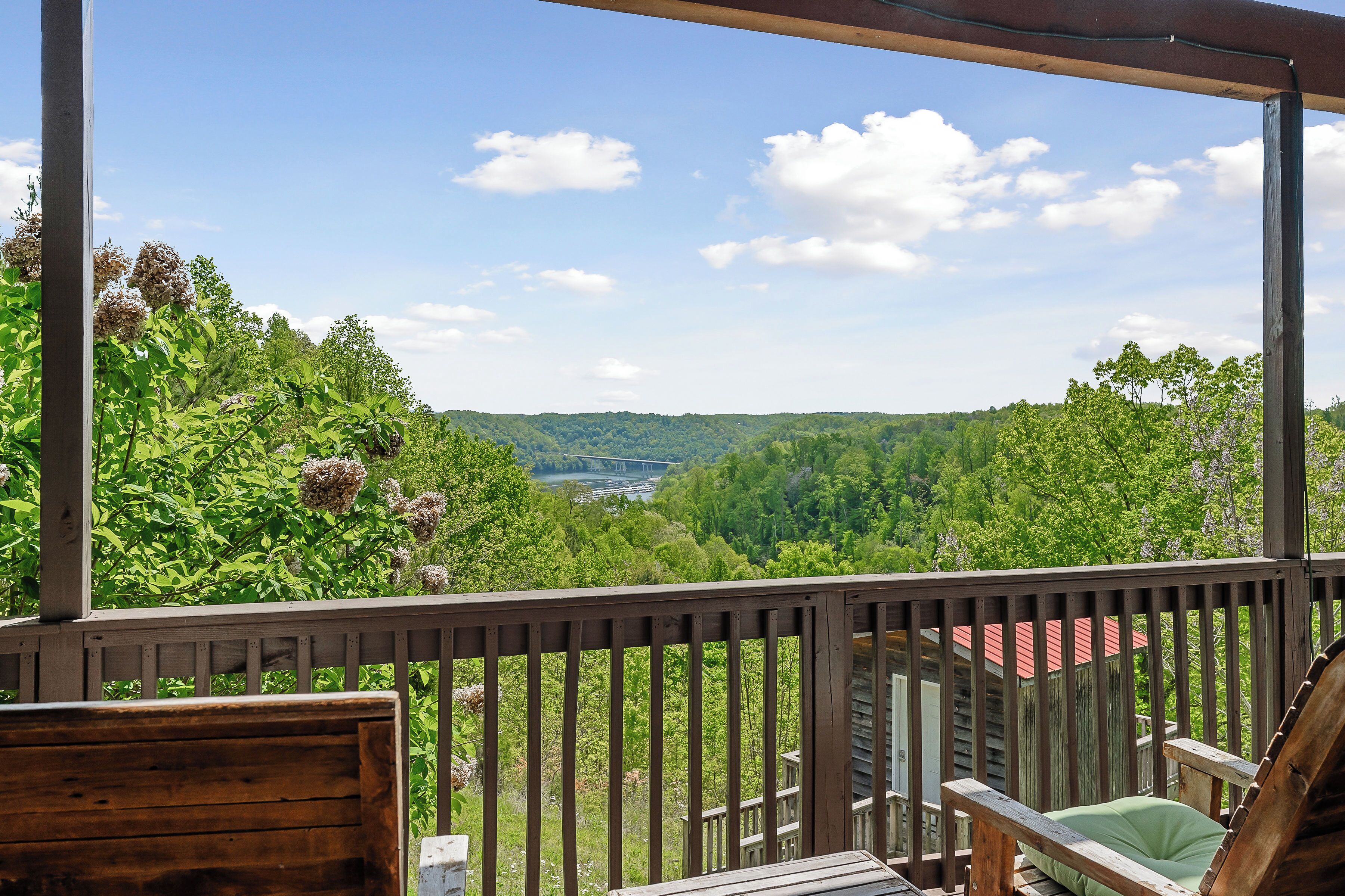 A wooden deck with a view of a green valley and a bridge in the distance.