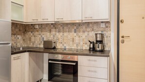 Una cocina compacta con armarios de madera clara, un backsplash estampado, un tostador, una cafetera y un horno empotrado.