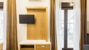 Una habitación de hotel moderna con un mueble de televisión de madera, un televisor de pantalla plana, una pequeña zona de estar y una puerta de vidrio corredera al exterior.