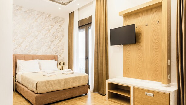 Una habitación de hotel moderna con una cama grande, un televisor montado en un panel de madera y un banco de madera.