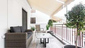 Un balcón con mobiliario de mimbre, una mesa y plantas en macetas.
