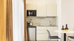 Cocina compacta con microondas, cafetera y lavavajillas. Cuenta con una mesa de comedor con dos sillas y dos jarrones decorativos.