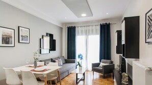 Ein modernes Wohnzimmer mit Essbereich, einer Couch, einem Couchtisch und einem Fernseher auf einem Lowboard.