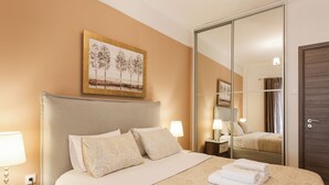 A hotel room with a large bed, a nightstand with a lamp, a wardrobe, and a painting on the wall.