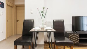 Un comedor moderno con una mesa de vidrio, dos sillas de cuero negro, un jarrón con flores y un televisor sobre un mueble negro.
