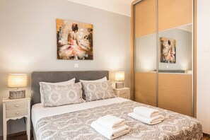 A neatly made bed with patterned bedding, two bedside lamps, and a large mirror cabinet.