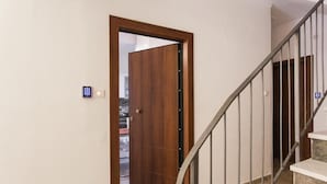 Une porte en bois dotée d’un clavier pour l’ouverture, un escalier en métal et, au fond, une cuisine visible.