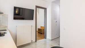 A modern room with a flat-screen TV mounted on the wall, a radiator, and a wooden bench in the background. - Oasis apartment suite (ATHENS)