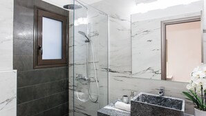 A modern bathroom with a glass-enclosed shower, a marble-tiled wall, a sink with a marble countertop, and a mirror. - Romantic Studio in the Heart of Athens (ATHENS)
