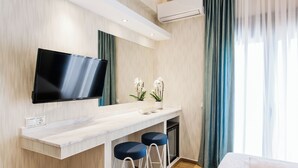 A modern hotel room with a flat-screen TV mounted on the wall, a marble countertop, two bar stools, a bed with a white comforter, and a large window with sheer curtains. - Romantic Studio in the Heart of Athens (ATHENS)