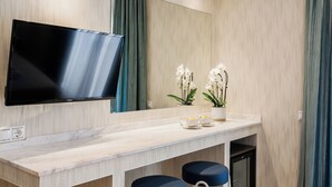 A modern bathroom with a large mirror, a flat-screen TV, a marble countertop, two blue stools, and potted orchids. - Romantic Studio in the Heart of Athens (ATHENS)