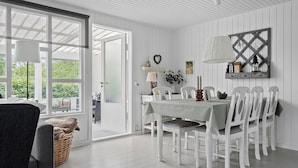 A dining area with a table set for six, white chairs, a chandelier, and a view through the open door.