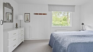 A bedroom with a bed, dresser, mirror, lamp, and window with a view of greenery.