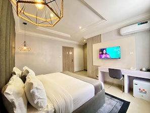 A modern hotel room with a large bed, a desk, a television, and a ceiling light fixture. - Bomma Residencies  (Abuja)