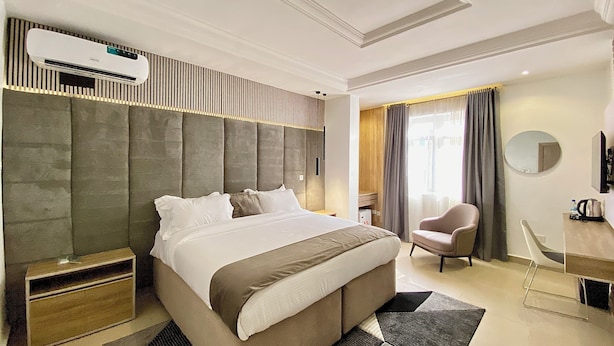 A modern hotel room with a large bed, a desk, a chair, and an air conditioning unit. - Bomma Residencies  (Abuja)