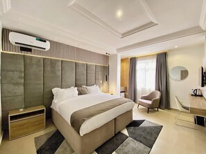 A modern hotel room with a large bed, a desk, a chair, and an air conditioning unit. - Bomma Residencies  (Abuja)