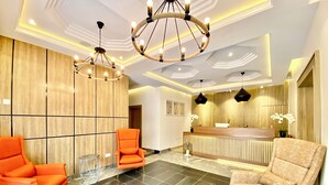 A modern reception area with a wooden reception desk, two orange chairs, and a marble floor. - Bomma Residencies  (Abuja)