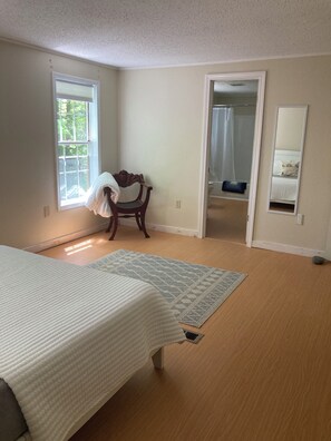 Une chambre à coucher comprenant un lit, une chaise, une fenêtre, une porte donnant sur une salle de bain et un miroir.