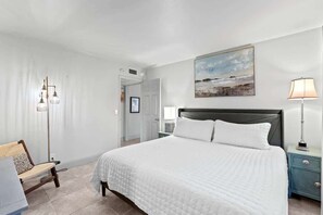 Un dormitorio con una cama grande, una mesita de noche, una silla y una lámpara de pie.