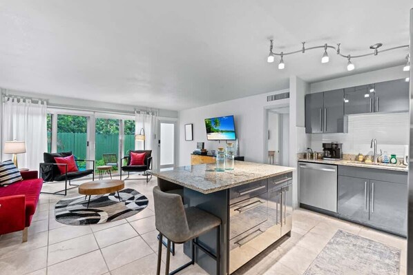 Una cocina moderna con electrodomésticos de acero inoxidable, una isla central y un comedor con sofá rojo y alfombra estampada en blanco y negro.