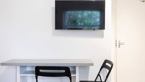 Ett rum med en vit dörr, en platt-TV som är monterad på väggen, ett grått bord och två svarta stolar.