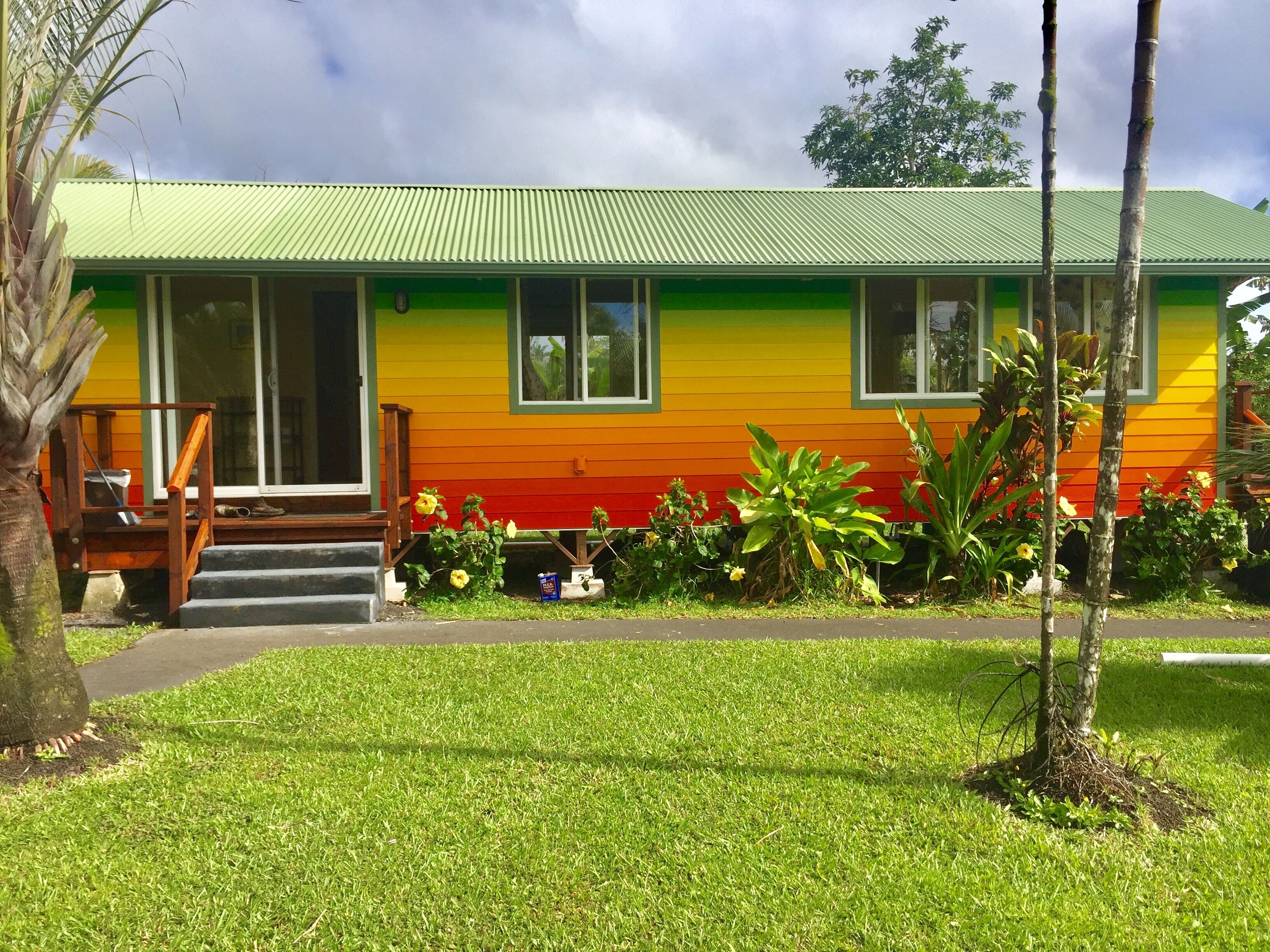 A colorful house with a green roof, a porch with wooden steps, and a well-maintained lawn.