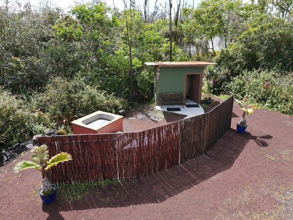 A small outdoor area with a wooden fence, a small green structure with a bench, and two potted plants.