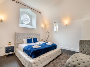 A bedroom with a large bed, a nightstand, a chair, and a window with a view of trees.